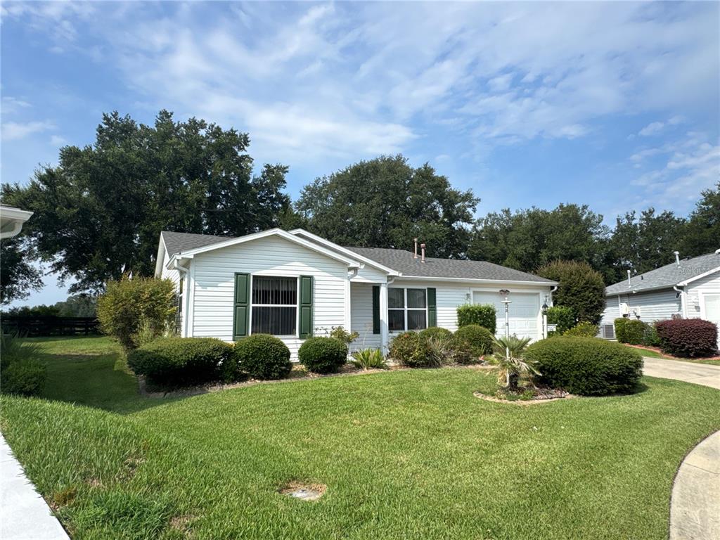 A single-story white house with green shutters and a front lawn under a blue sky — 17481 SE 76TH FLINTLOCK TERRACE, THE VILLAGES, FL
