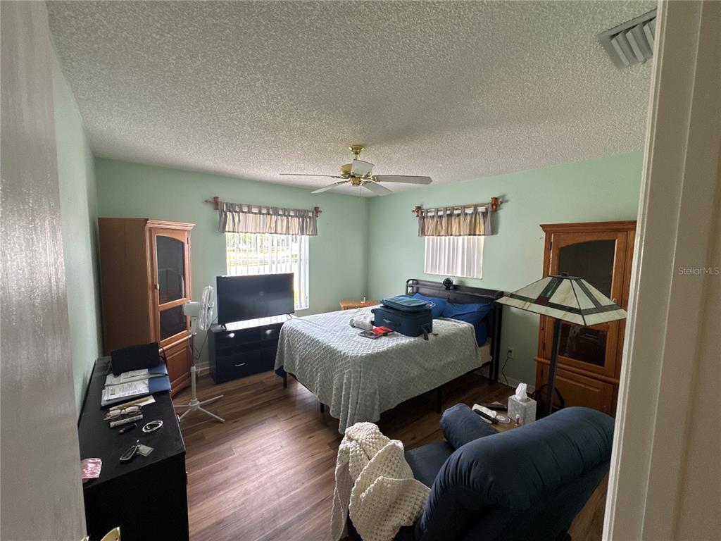 A bedroom features light green walls, wood-look flooring, a ceiling fan, and two wooden armoires — 17481 SE 76TH FLINTLOCK TERRACE, THE VILLAGES, FL