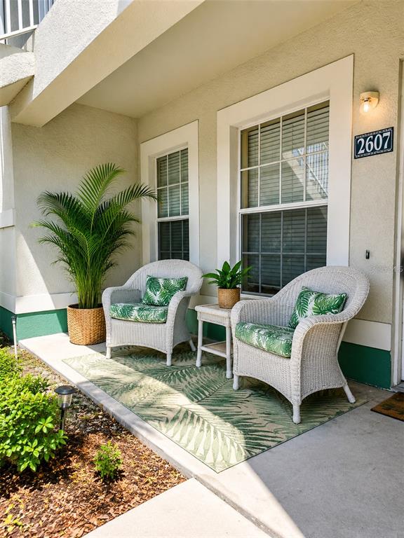 A covered patio features two white wicker chairs with green palm-print cushions on a rug — 2607 RIVER PRESERVE COURT UNIT 2607, BRADENTON, FL