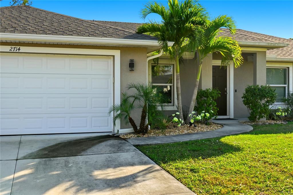 A single-story house exterior features a white garage door, a front entrance, and palm trees — 2714 NW 22ND TERRACE, CAPE CORAL, FL