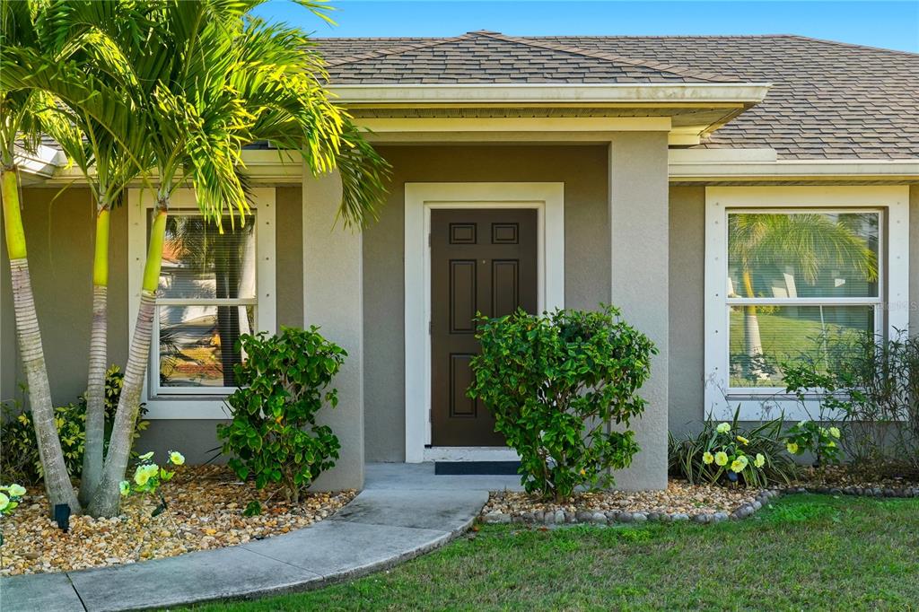 The exterior of a house features a brown front door, two windows, and palm trees — 2714 NW 22ND TERRACE, CAPE CORAL, FL