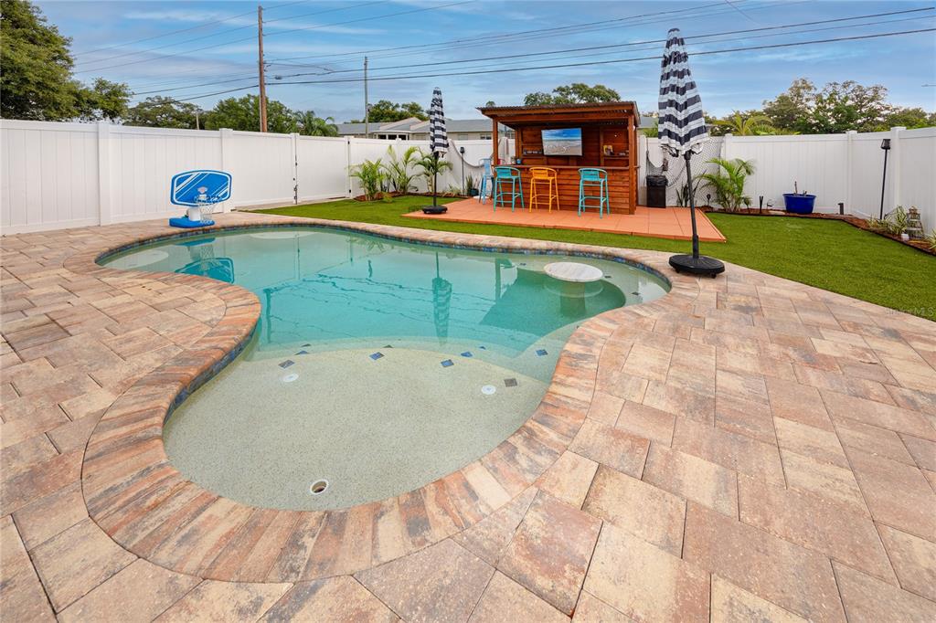 A backyard featuring a swimming pool, a paved patio, and a wooden outdoor bar area — 6200 52ND AVENUE N, ST PETERSBURG, FL