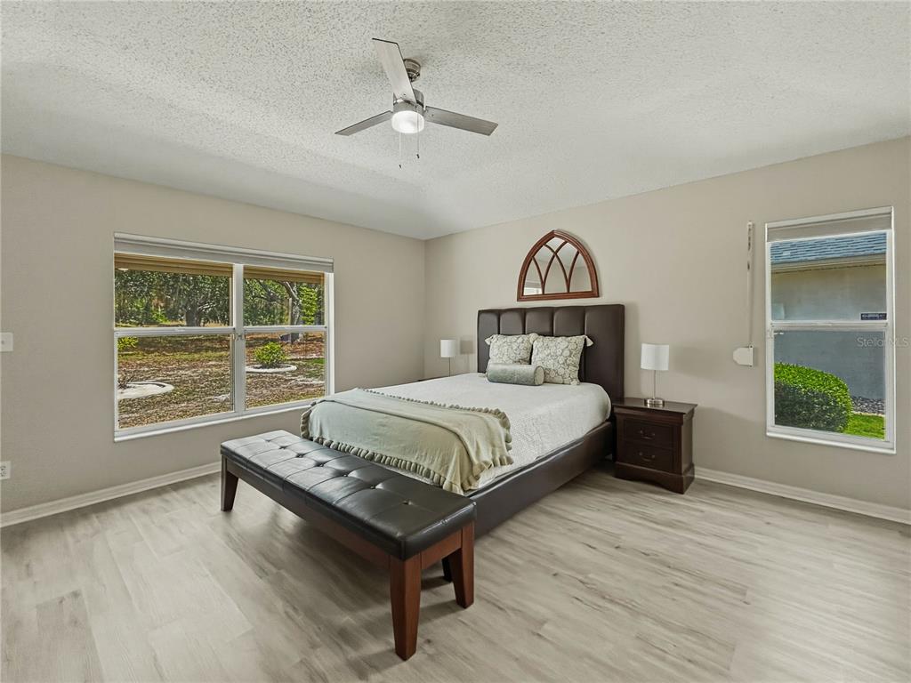 A bedroom features light wood-look flooring, a dark upholstered bed, and a ceiling fan — 2309 E DEL WEBB BOULEVARD, SUN CITY CENTER, FL