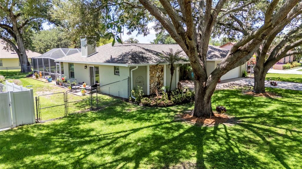 An exterior view of a single-story house with a fenced yard and large oak trees — 422 WILLOW RUN, LAKELAND, FL