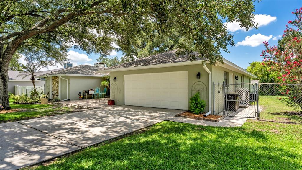 A light green house with a white garage door and a concrete driveway under trees — 422 WILLOW RUN, LAKELAND, FL