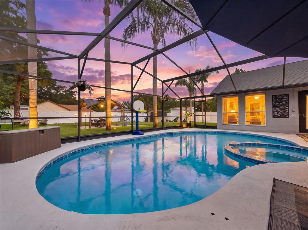 A screened-in swimming pool and spa area with a sunset view in the backyard — 5014 SAWDUST CIRCLE, OCOEE, FL