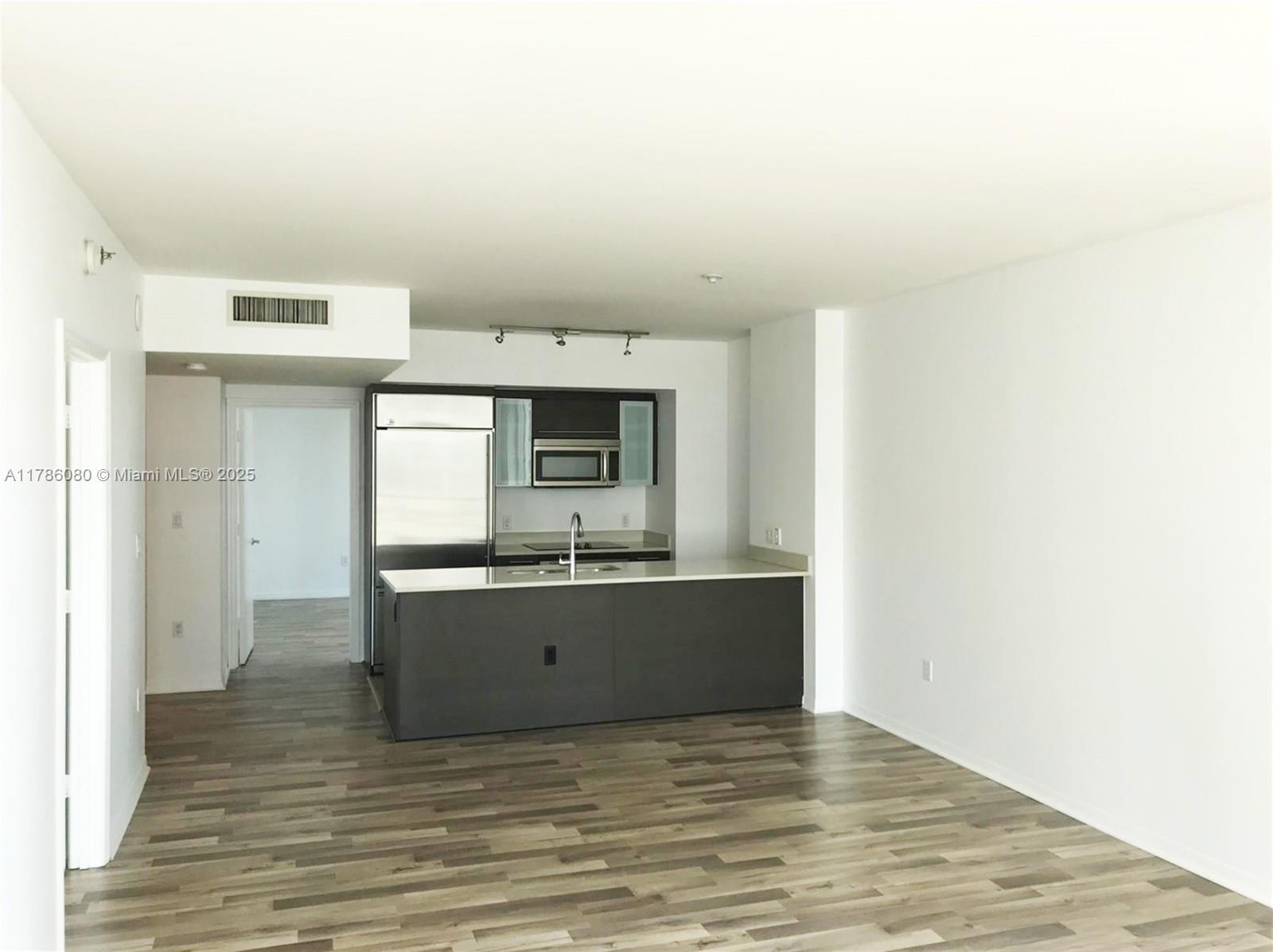 An open-concept kitchen with dark cabinetry and stainless steel appliances overlooks a living area — 55 SE 6th St # 1610, Miami FL 33131, MIAMI, FL