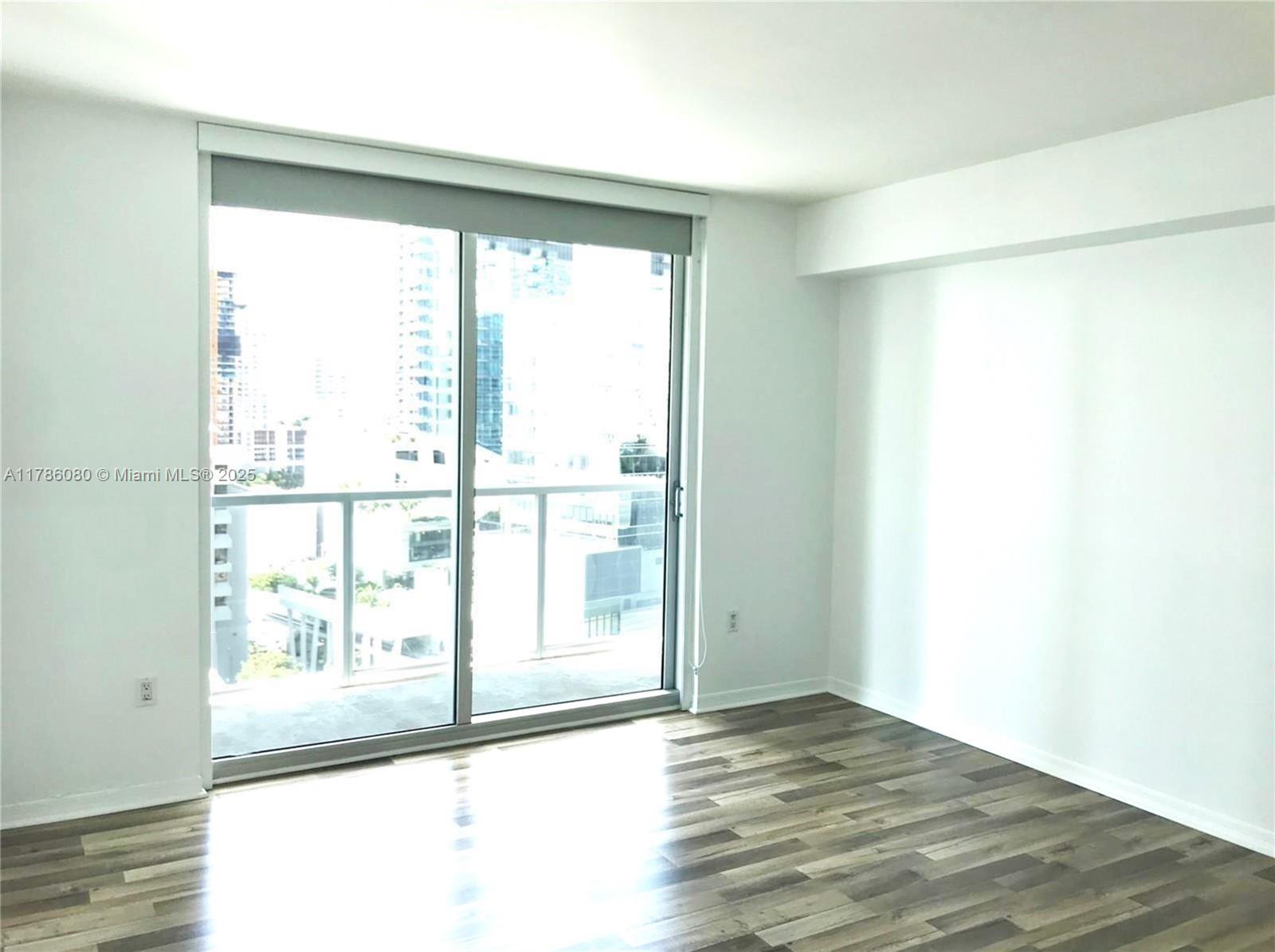 An empty room features white walls, wood-look flooring, and a sliding glass door to a balcony — 55 SE 6th St # 1610, Miami FL 33131, MIAMI, FL