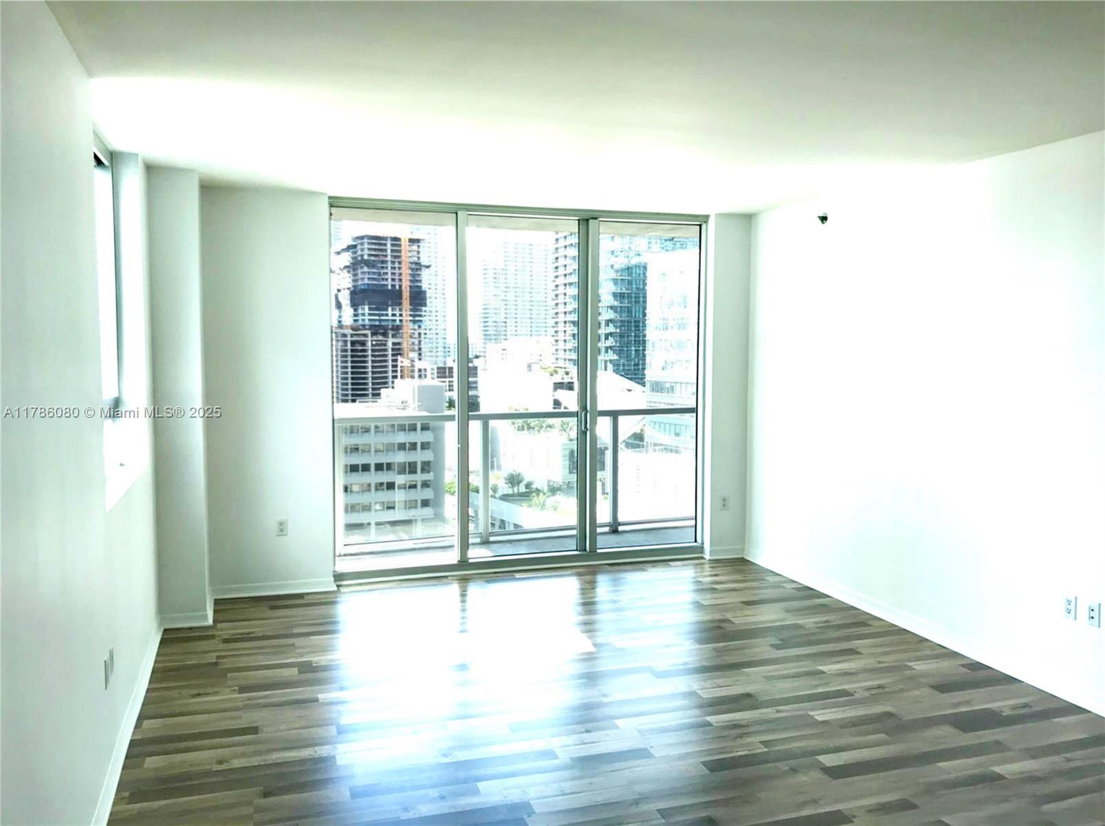 An empty room features wood-look flooring, white walls, and a large sliding glass door balcony — 55 SE 6th St # 1610, Miami FL 33131, MIAMI, FL