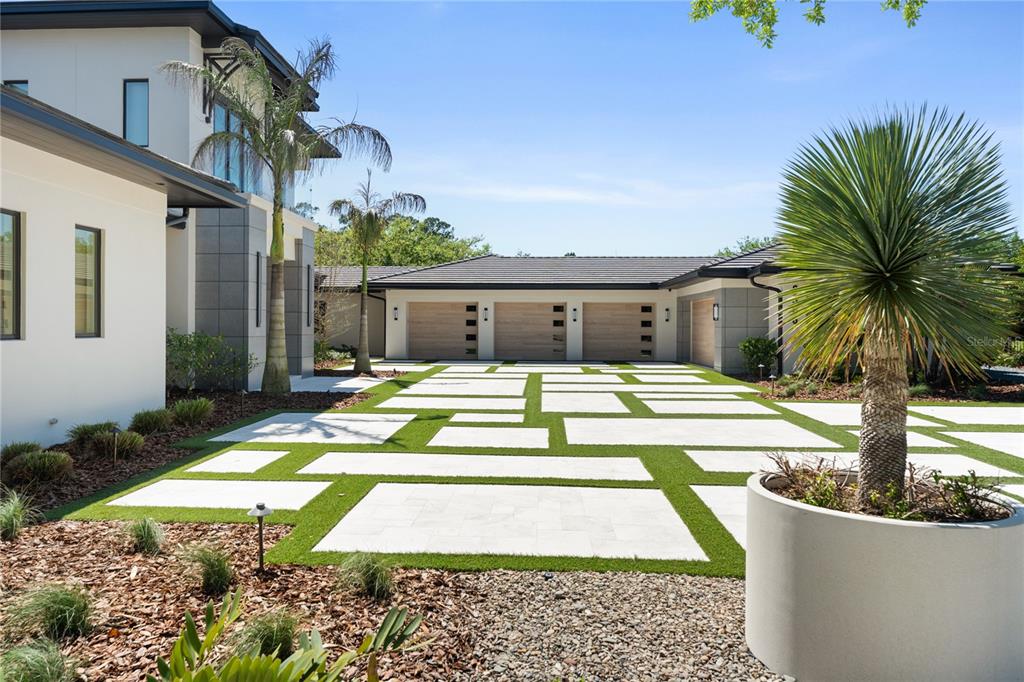 A modern house exterior features a multi-car garage and a geometric paver driveway with grass — 8506 LAKE NONA SHORE DR, ORLANDO, FL