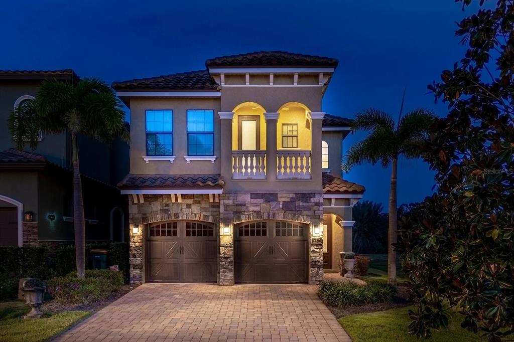 A two-story house with a stone facade, two garage doors, and an upper-level balcony at dusk — 717 DESERT MOUNTAIN COURT, REUNION, FL