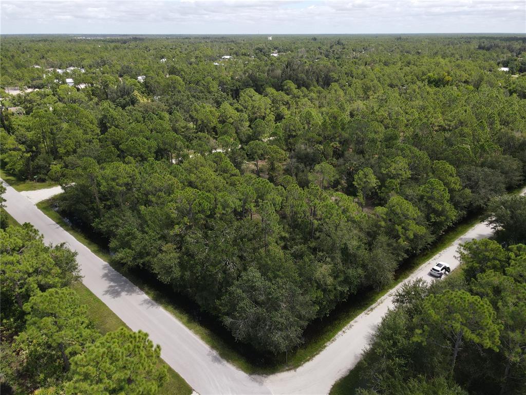 An aerial view shows a wooded, undeveloped corner lot bordered by two paved roads — 27282 ALOHA DRIVE, PUNTA GORDA, FL