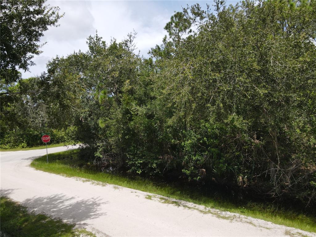A dirt road curves past a dense, wooded lot with a stop sign visible — 27282 ALOHA DRIVE, PUNTA GORDA, FL