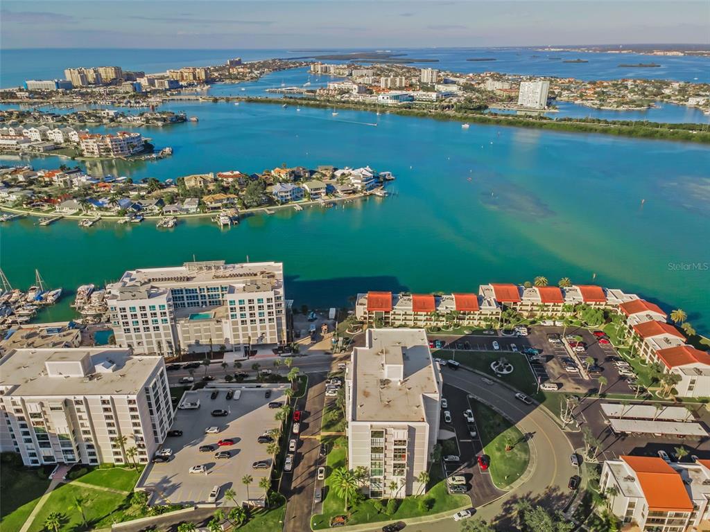 An aerial view shows waterfront apartment buildings with parking lots and a large bay — 855 BAYWAY BOULEVARD UNIT 708, CLEARWATER BEACH, FL