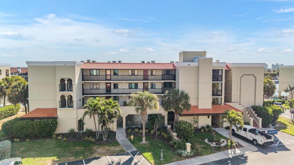 A multi-story apartment building with a tiled roof, balconies, and palm trees in the foreground — 7435 BAYSHORE DRIVE UNIT 303, TREASURE ISLAND, FL