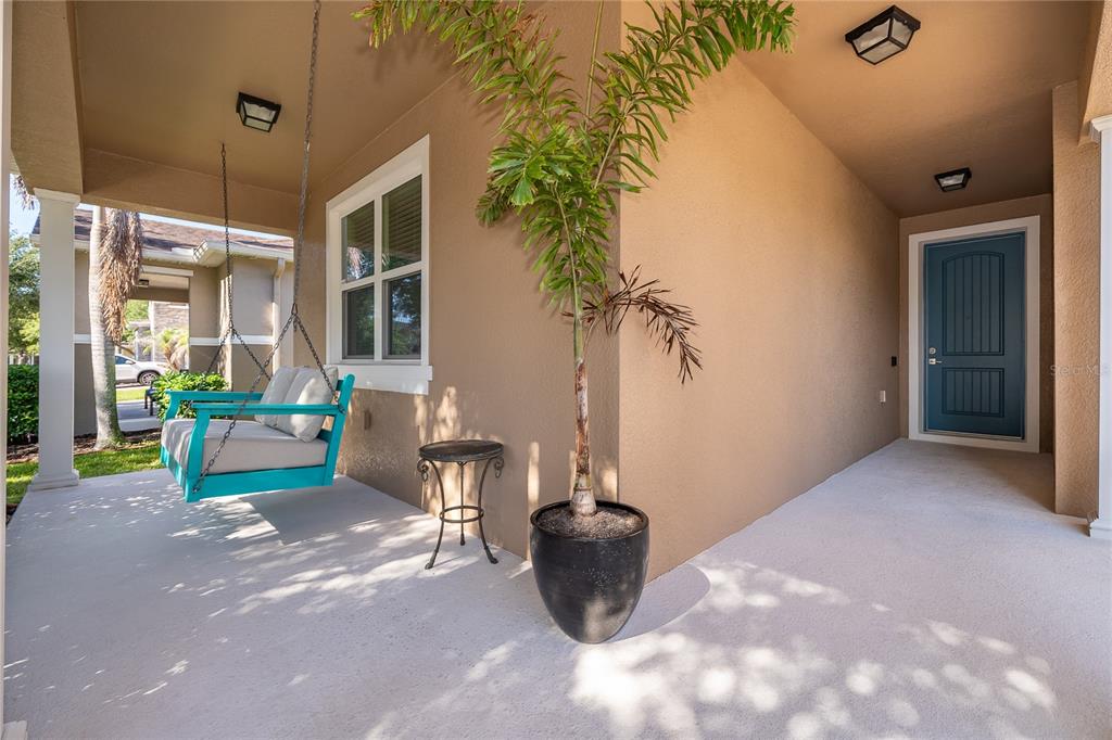 A covered porch features a teal hanging swing, a potted palm, and a blue door — 11437 WAKEWORTH STREET, ORLANDO, FL