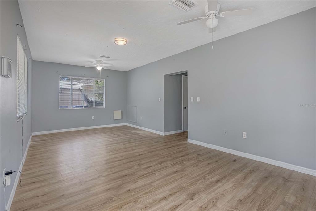 An empty room with gray walls, light wood-look flooring, and two ceiling fans — 1416 19TH AVENUE W, BRADENTON, FL