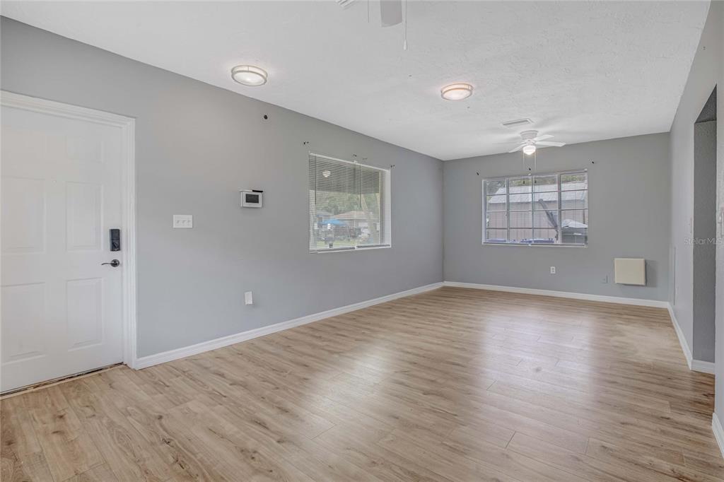 An empty living room features light gray walls, wood-look flooring, two windows, and a ceiling fan — 1416 19TH AVENUE W, BRADENTON, FL
