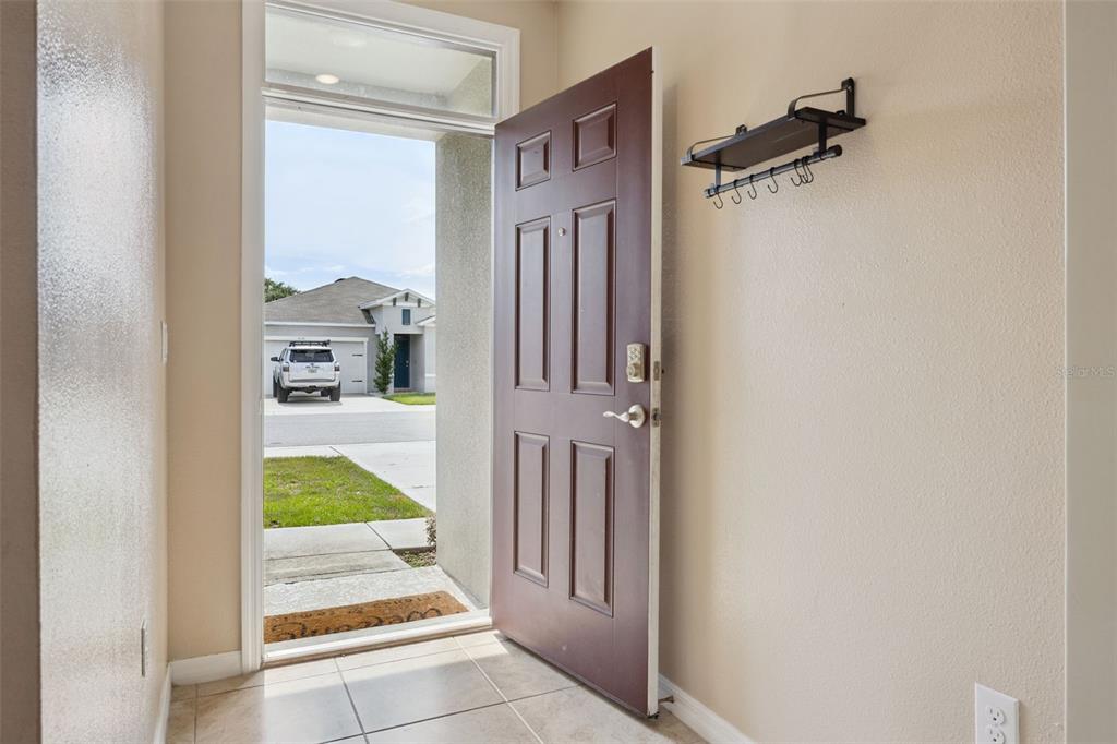 An open front door reveals a tiled entryway with a wall-mounted coat rack — 511 JACKS WAY, DAVENPORT, FL