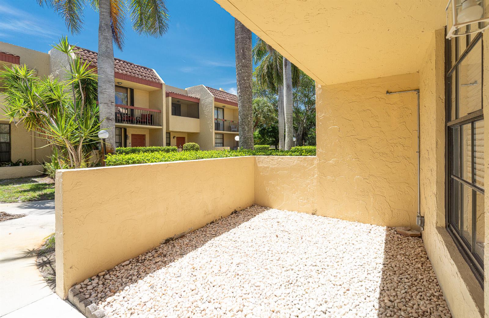 A small, gravel-covered patio with a low stucco wall sits outside a tan building — 769 SE 1st Way # 85, Deerfield Beach FL 33441, DEERFIELD BEACH, FL