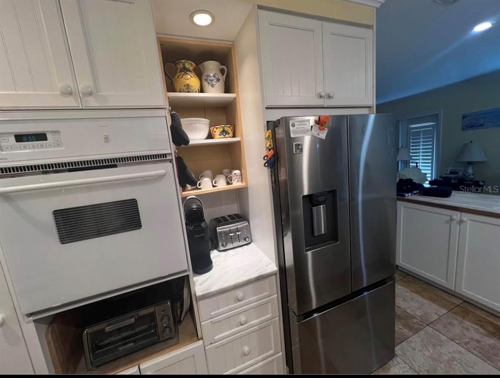 A kitchen features white cabinetry, a stainless steel refrigerator, and a built-in wall oven — 5164 BEACH DRIVE SE UNIT B furnished, ST PETERSBURG, FL