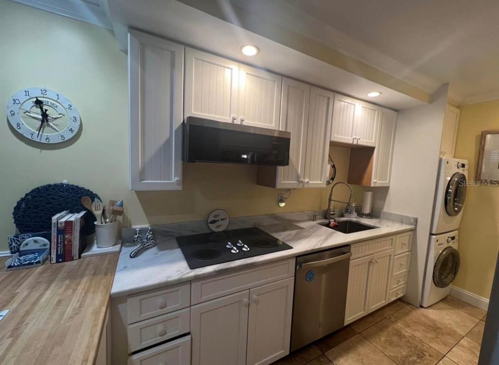 A kitchen features white cabinets, a black cooktop, stainless steel appliances, and a marble countertop — 5164 BEACH DRIVE SE UNIT B furnished, ST PETERSBURG, FL