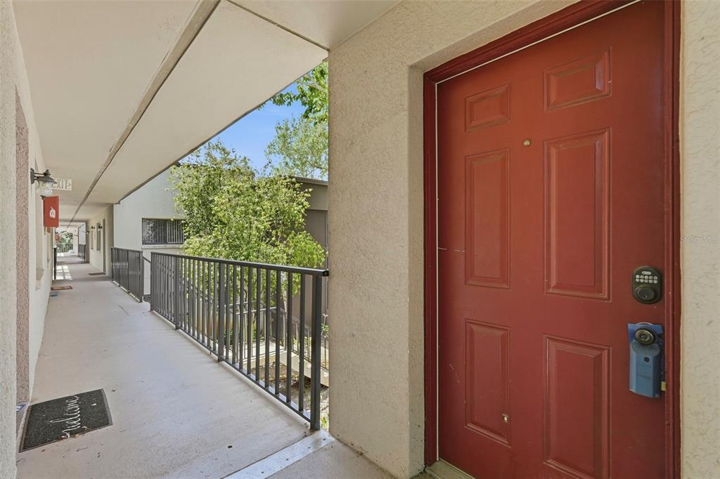 A red door with a keypad lock opens onto an outdoor apartment building walkway — 11709 RAINTREE VILLAGE BOULEVARD UNIT C, TEMPLE TERRACE, FL