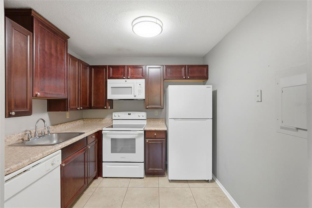 A kitchen features dark wood cabinets, white appliances, beige countertops, and light tile flooring — 11709 RAINTREE VILLAGE BOULEVARD UNIT C, TEMPLE TERRACE, FL
