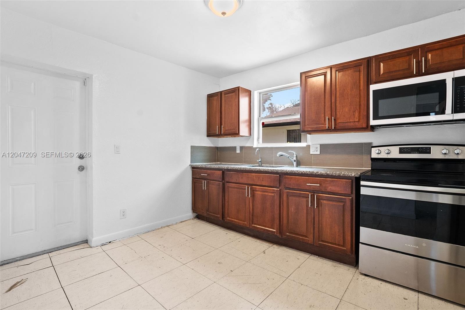 A kitchen features wood cabinets, stainless steel appliances, a window, and light-colored tile flooring — MIAMI, FL