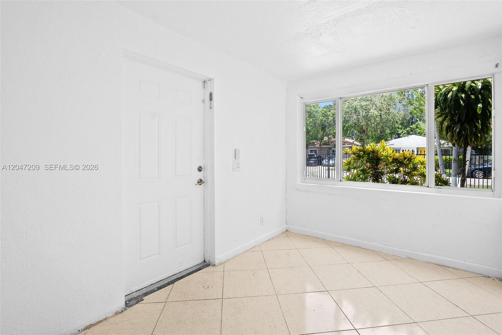 A bright, empty room features white walls, light-colored tile flooring, and a large window — MIAMI, FL