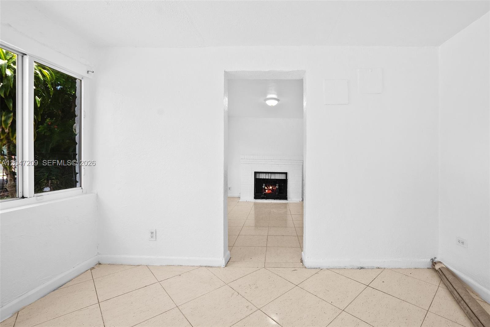 A room with light-colored tile flooring leads through an arched doorway to a fireplace — MIAMI, FL
