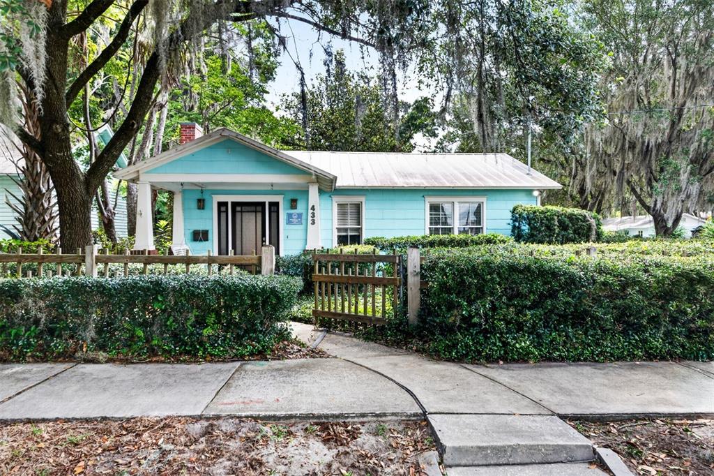 A light blue cottage with a front porch and a wooden fence sits behind hedges — 433 SE 7TH STREET, GAINESVILLE, FL