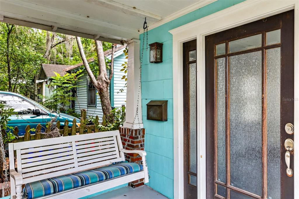 A white porch swing sits on a covered porch with teal siding and a glass door — 433 SE 7TH STREET, GAINESVILLE, FL