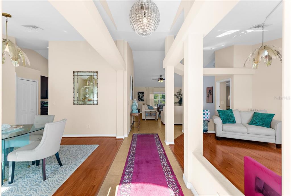 A bright, open-concept living and dining area features hardwood floors, a purple runner, and chandeliers — 8431 WALDREP STREET, PORT CHARLOTTE, FL