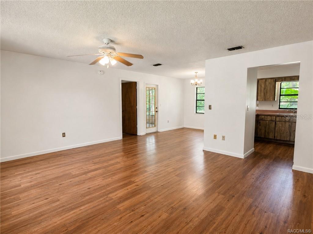 An open-concept living area features wood-look flooring, white walls, a ceiling fan, and an adjacent kitchen — 3565 E PERRY STREET, INVERNESS, FL