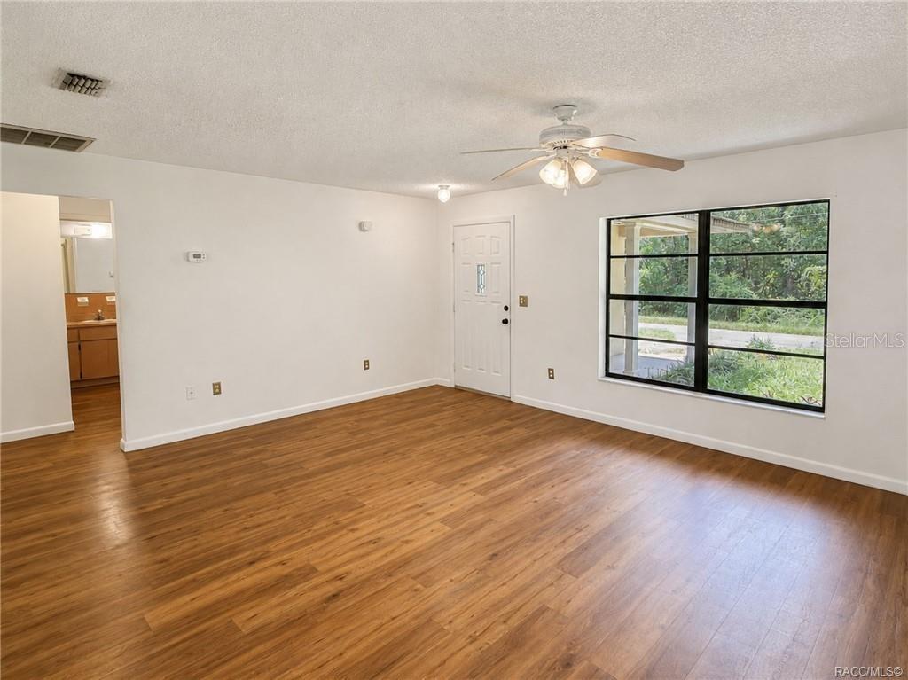 A living room with white walls, wood-look flooring, a ceiling fan, and a large window — 3565 E PERRY STREET, INVERNESS, FL