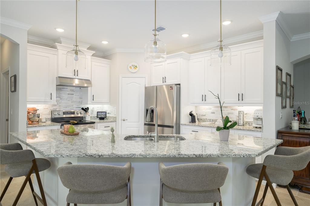 A kitchen features white cabinets, granite countertops, a large island with seating, and stainless appliances — 25 EDGE LANE, PALM COAST, FL