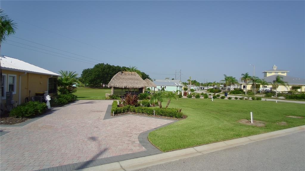 A paved driveway leads to a grassy yard featuring a thatched-roof tiki hut structure — 3063 WOOD DUCK DRIVE, POLK CITY, FL