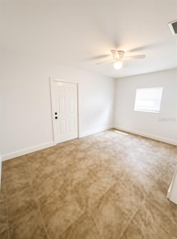 An empty room features white walls, a ceiling fan, a white door, and tiled flooring — 1125 13TH AVENUE S, ST PETERSBURG, FL