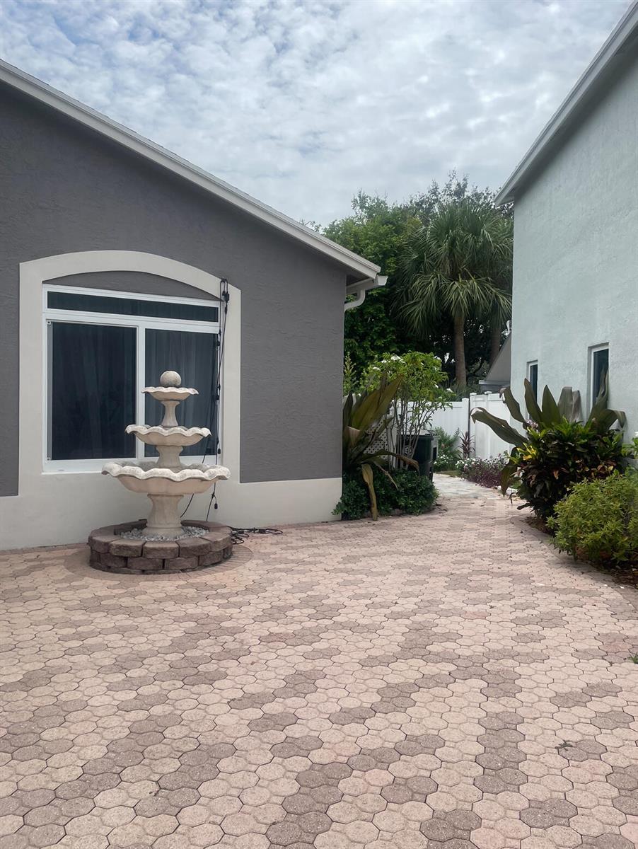 A stone fountain sits on a paved patio between two residential houses — 4251 Pine Hollow Circle, FL 33463, FL