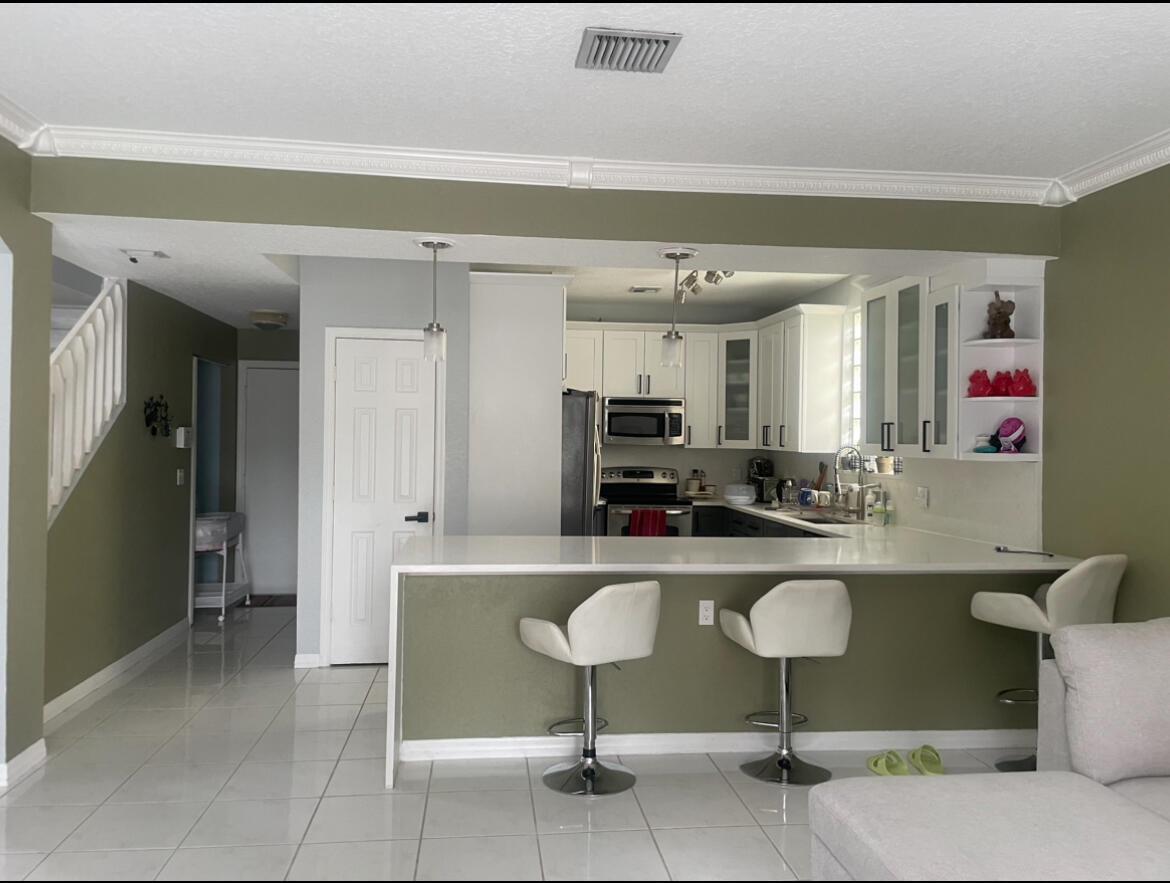 A kitchen with white cabinets and a peninsula breakfast bar overlooks a living area — 4251 Pine Hollow Circle, FL 33463, FL