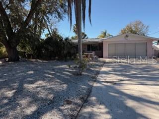 A single-story house with a light-colored exterior and a multi-car garage sits behind a driveway — 7127 PENINSULAR DRIVE, NEW PORT RICHEY, FL