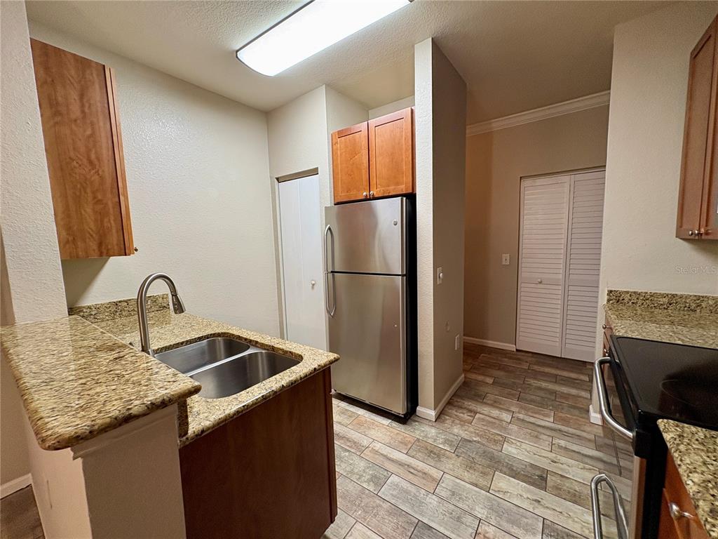 A kitchen features stainless steel appliances, granite countertops, wood cabinets, and wood-look tile flooring — 2171 PORTOFINO PLACE UNIT 2714, PALM HARBOR, FL