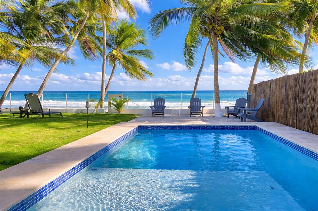 A swimming pool sits in a backyard overlooking the ocean with palm trees and chairs — STREET NO 3 KM 112 BO. GUARDARRAYA, PATILLAS, PR