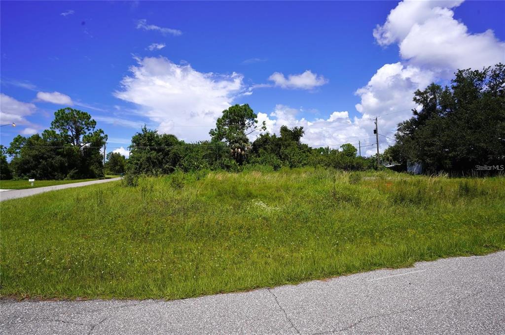 A vacant, grass-covered corner lot with trees and a paved road in the foreground — 12342 GABRIEL AVENUE, PORT CHARLOTTE, FL