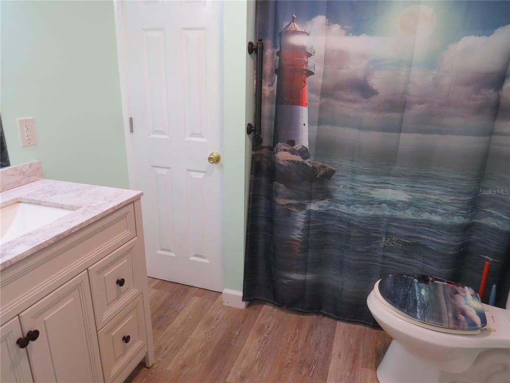 A bathroom features a vanity with a marble-look countertop, wood-look flooring, and a lighthouse shower curtain — 705 BLACKBURN BOULEVARD, NORTH PORT, FL
