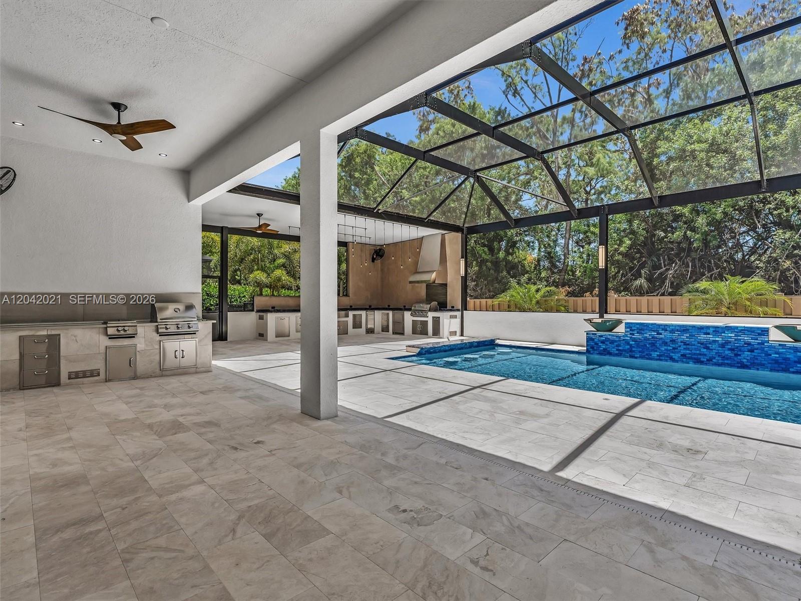 A covered patio features a swimming pool, outdoor kitchen, and a screened-in enclosure — 7680 Cavern Ln, Parkland FL 33067, PARKLAND, FL