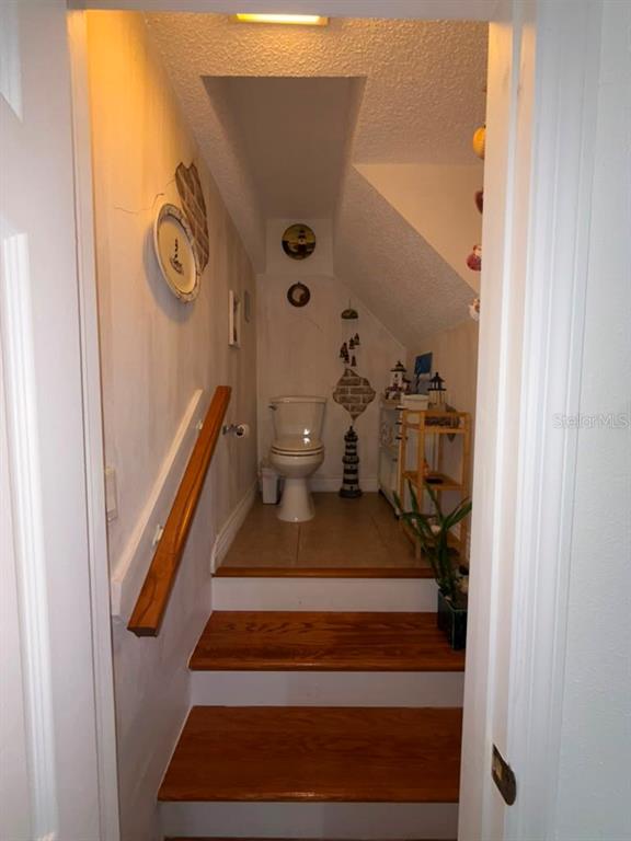 A small bathroom with a toilet is situated at the top of a wooden staircase — 6648 TIMBERCOVE LANE UNIT 6648, NEW PORT RICHEY, FL