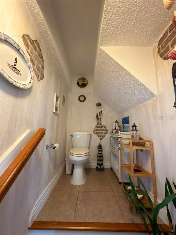 A small bathroom features a toilet, tile flooring, and nautical-themed decor under a sloped ceiling — 6648 TIMBERCOVE LANE UNIT 6648, NEW PORT RICHEY, FL