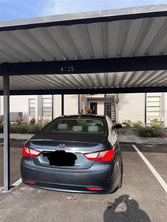 A dark gray sedan is parked under a covered carport in front of an apartment building — 4725 PURITAN CIRCLE UNIT 603, TAMPA, FL